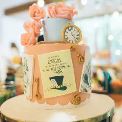 A cake that tells a story. This Alice in Wonderland cake is adorned with edible details like the Mad Hatter's famous quote, a pocket watch, and delicate sugar roses, making it a true work of art.
