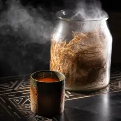 A dark and moody shot of a steaming, spiced beverage. The contrast between the dark background and the rising steam creates a sense of warmth and mystery.