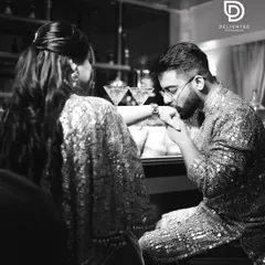 A classic romantic gesture captured in timeless black and white, as the groom kisses the bride's hand during their engagement party.