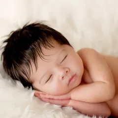 The classic 'tushy up' pose on a soft, white fur blanket. This is a parent favorite, showcasing the baby's smooth skin and the peacefulness of their sleep.