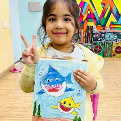 Look at this proud artist with her fantastic shark drawing! Our creative art sessions are all about letting kids explore their imagination and express themselves through color and paint, no matter how messy it gets.