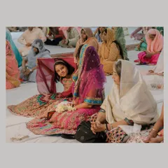 A candid shot of guests, including a young girl looking back at the camera, during a Gurudwara ceremony, capturing the atmosphere of the gathering.