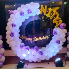 A beautiful birthday ring decoration in white and purple, perfect for a home setup. The foil name balloon and 'Happy Birthday' banner make it a personalized photo corner.