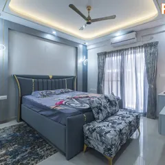 A modern bedroom design in a cool blue and grey palette with subtle gold accents. The false ceiling with cove lighting and stylish butterfly-shaped wall sconces add a touch of glamour and sophistication.