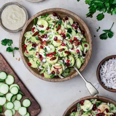 A fresh and vibrant cucumber salad with pomegranate and almonds, presented in a rustic wooden bowl.