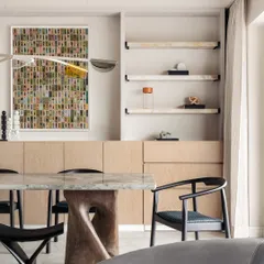 A closer look at the dining area in Apartment O2. The design is a harmony of clarity and warmth, with a glass and wood table base and colorful artwork.