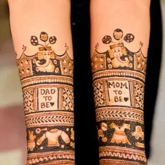 This design celebrates both parents with "Dad to be" and "Mom to be" blocks, topped with a cute Ganesha motif and surrounded by baby clothes and toy patterns.