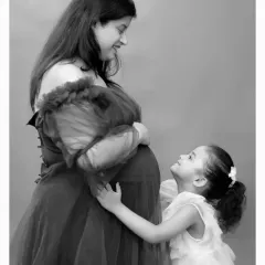 A sweet black and white photo of an older sister looking up lovingly at her mother's baby bump, capturing the anticipation of a new sibling.