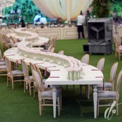 A stunning serpentine table decorated with a continuous line of single pink roses in glass vases. This simple yet impactful design creates a beautiful and romantic focal point in the reception space.