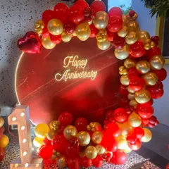 I design bold and beautiful backdrops to celebrate your special milestones. This first-anniversary setup features a vibrant red circular panel, a custom 'Happy Anniversary' neon sign, and a lush garland of red and gold balloons, complete with an illuminated number '1'.