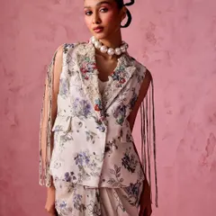 A modern take on ethnic wear. This floral print ensemble features a draped skirt and a sleeveless blazer with dramatic fringe details, paired with a statement pearl choker.