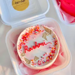 A close-up of the personalized "Rashmi" bento cake from the set, featuring colorful sprinkles and gold leaf for a celebratory touch.