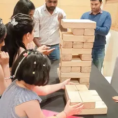 Guests gathered around a table playing Giant Jenga indoors at a birthday party. This game is versatile and can be set up in almost any event space.