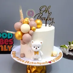 A chic and modern baby shower cake in neutral tones, featuring a textured teddy bear and a cascade of edible chocolate spheres.