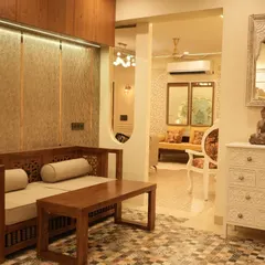 This living space features a classic carved wooden sofa and coffee table. The design is complemented by a vintage-style white chest of drawers and patterned floor tiles, creating a charming, old-world feel.