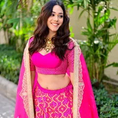A candid moment of laughter is sometimes the most beautiful shot. Here, the vibrant pink of the bandhani lehenga comes alive against the green backdrop, showcasing a perfect blend of traditional wear and joyful expression.