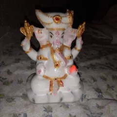 A small, intricately detailed statue of Lord Ganesha in white and gold, suitable for a home altar or as a decorative piece.