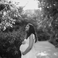A gorgeous black and white portrait of a mother-to-be in a garden. She looks up towards the light with a hopeful and happy expression, full of anticipation.