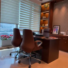 Another perspective of the executive office, showing the relationship between the main desk, visitor chairs, and the custom-built storage unit. The large windows with blinds allow for controlled natural light.