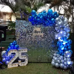 We take the party outdoors with this bold and vibrant setup on a lawn. A deep blue shimmer wall is framed by an arch of metallic blue and silver balloons, complemented by light-up marquee numbers to celebrate a milestone 25th birthday.