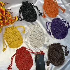 A beautiful assortment of my crochet potli bags laid out next to a phone for size reference. You can see them in various glittery yarns like black, orange, purple, yellow, red, and brown, showing the range of colors available.