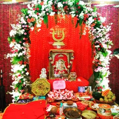 A beautiful home setup for Mata Rani celebrations. The altar is decorated with a dense floral arch of red and white flowers against a rich red backdrop, complete with all the traditional offerings.