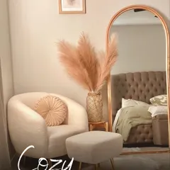 Creating a cozy corner is all about soft textures and warm lighting. This plush armchair, paired with a fluffy ottoman, pampas grass, and an arched mirror, creates the perfect nook for relaxation.