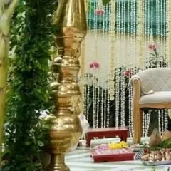 A close-up of a traditional wedding mandap. The decor includes elegant seating, brass elements, and a backdrop made of beautiful jasmine flower strings.