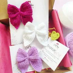 Our classic crochet Sailor Bows, shown here in magenta, white, and lavender. They are attached to clips and are a versatile accessory that fits all and suits all.