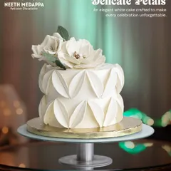 The 'Dance of Delicate Petals' is an elegant all-white celebration cake. The unique, folded petal texture around the tiers creates a sense of movement and sophistication, topped with delicate white sugar flowers.