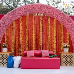 A classic Mehendi seating area featuring a backdrop of orange and yellow marigold strings and a plush pink sofa, perfect for the bride.