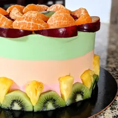 A side view of the fresh fruit cake, showing the colorful layers of frosting and the border of sliced kiwi and pineapple.
