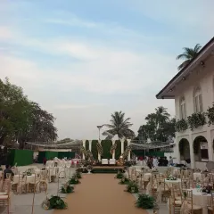 A daytime view of the reception setup, showing the grand scale of the event. The long aisle leads to a large stage against a green backdrop, with seating arranged for all guests to have a perfect view.
