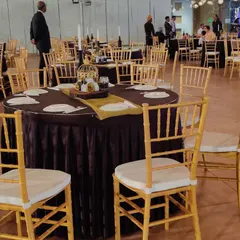 A closer look at a table setting for a formal corporate dinner. The use of dark, rich tablecloths with elegant gold Chiavari chairs and simple centerpieces creates a classic and professional look suitable for any high-profile company function.