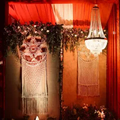 A beautiful backdrop combining rustic and elegant elements. We hung intricate macrame dreamcatchers against a wall of warm-toned drapes, crowned with greenery and a classic chandelier.