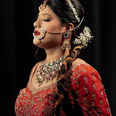 A serene and artistic bridal portrait. The bride's eyes are closed, drawing attention to her stunning makeup, traditional nath, and elaborate jewelry against a simple black backdrop.