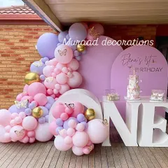This butterfly-themed first birthday is both whimsical and sweet. The setup features a large 'ONE' table for the cake, surrounded by a cascade of purple, pink, and gold balloons with delicate butterfly accents.