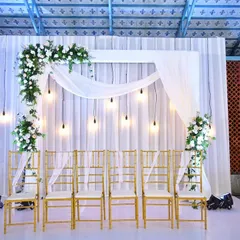 This elegant white-on-white backdrop is perfect for an engagement or a small, intimate wedding gathering. The clean drapes, hanging Edison bulbs, and asymmetrical floral arrangement create a modern and sophisticated look.