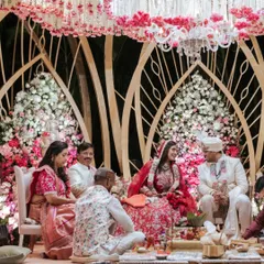 A couple during their wedding ceremony inside a Lotus-themed mandap. The intricate background structure and dense floral arrangements in pink and white create a divine setting.