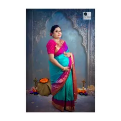 A full-length portrait from the same traditional maternity session. This pose beautifully showcases both the baby bump and the graceful drape of the saree, surrounded by festive elements like diyas and flowers.