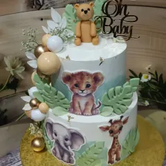 A sweet two-tiered baby animal cake for a baby shower or first birthday. It's decorated with adorable edible images of a lion cub, elephant, and giraffe, and topped with a fondant teddy bear.