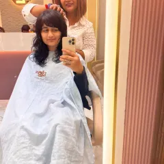 A client taking a mirror selfie of her new haircut. The fresh layers and bangs give her a modern and chic look.