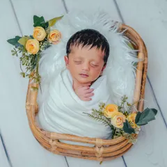 Simplicity and elegance define this newborn portrait. A pure white swaddle and delicate yellow flowers in a rustic basket create a fresh, clean look that focuses all the attention on the baby's serene features.