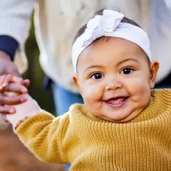 That big, gummy smile is just the best. This close-up captures the pure happiness of a baby who is learning to stand with a little help.
