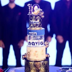 A towering four-tier cake for the 10th anniversary of the shipping company, NAVIO. This corporate cake features the company's branding, a black and gold color scheme, and an illuminated middle tier.