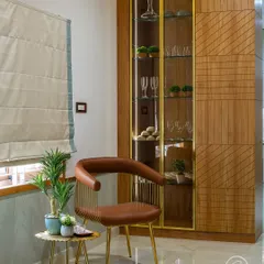 A custom-designed crockery unit with a glass front and gold metal frame. This elegant piece provides beautiful display storage for glassware and is complemented by a stylish leather and metal chair, creating a sophisticated corner.