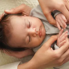 A close-up of a newborn being gently held by their parents' hands. This image, taken in soft natural light, captures the delicate features and tiny hands of the baby.
