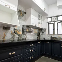 This kitchen combines classic and modern elements with dark navy shaker-style cabinets and a stunning marble-patterned backsplash. The gold handles add a touch of luxury, while the layout ensures everything is within easy reach.