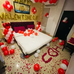Perfect for Valentine's Day, this decoration uses classic red and white balloons to fill the room with love. The design includes "Happy Valentine Day" foil letters and initials spelled out with rose petals on the floor.