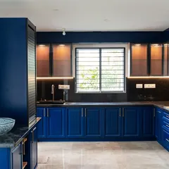 A bold and beautiful U-shaped kitchen with royal blue cabinets and a floral wallpaper accent wall. The fluted cabinet details and black granite countertop create a dramatic and sophisticated look.